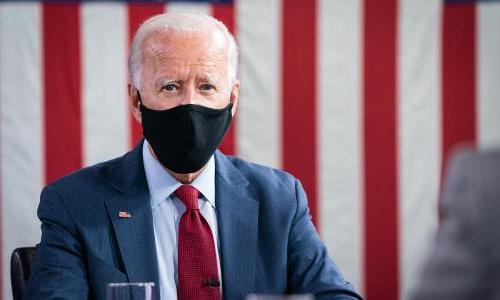Photo of presidential candidate Joe Biden sitting with a mask on and a flag-like red and white background